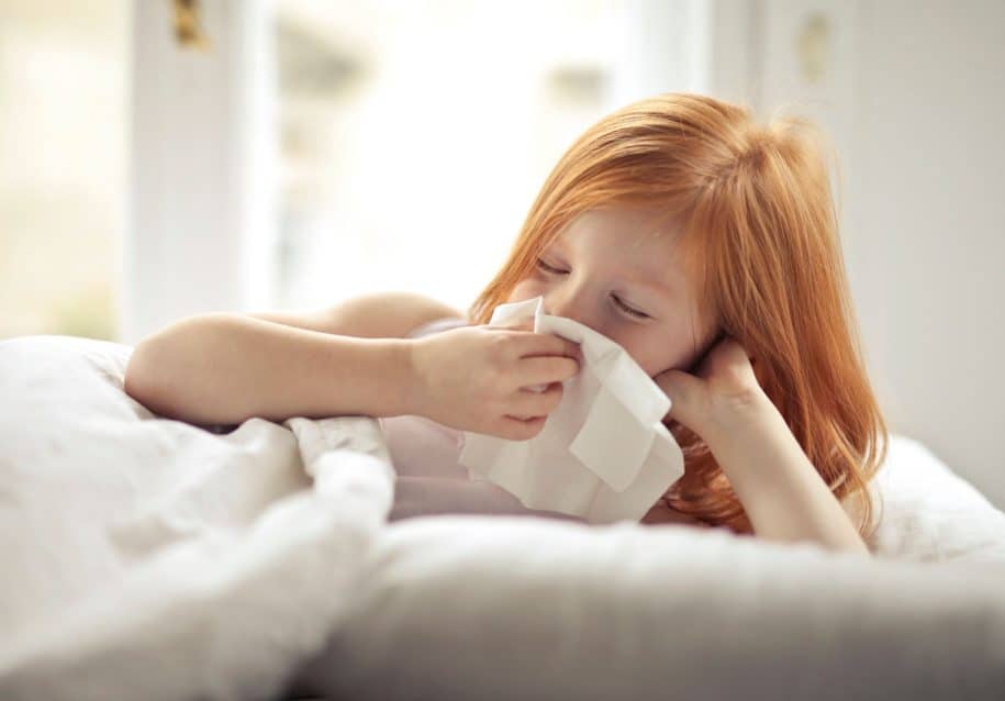 Young child blowing their nose into a tissue at home