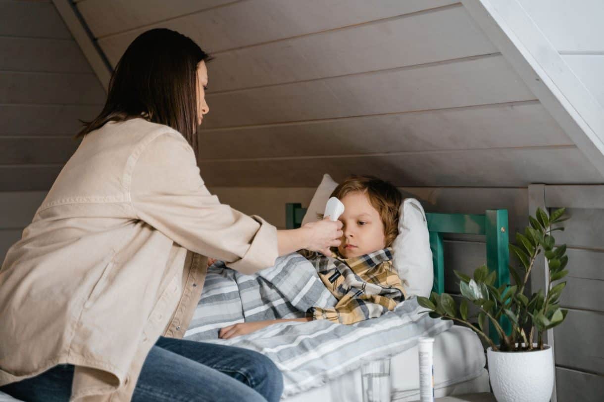 A mother placing her hand on her feverish child's forehead while the child rests