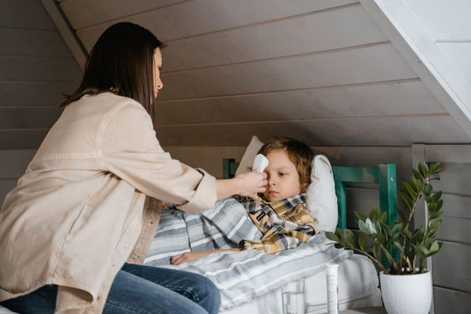 A mother placing her hand on her feverish child's forehead while the child rests